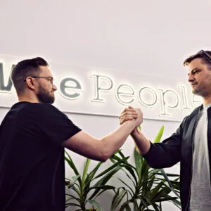 Developerzy Wise People zbijają piątkę po zakończonej pracy w nowoczesnym biurze, w tle widoczny jest neon z nazwą firmy.